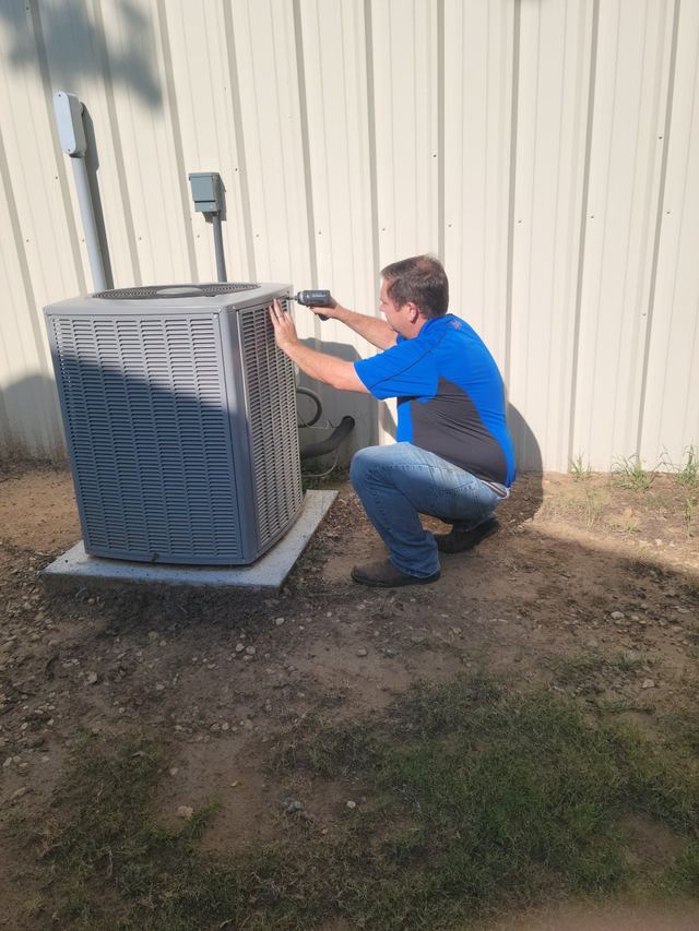 Technician kneeling beside an outdoor AC unit at a home