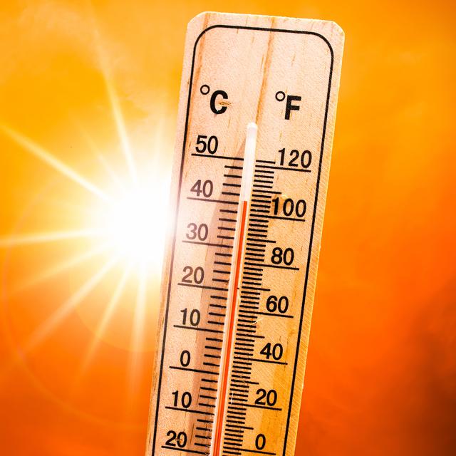Wooden thermometer reading about 100 degrees Fahrenheit against a bright orange sky with a blazing sun