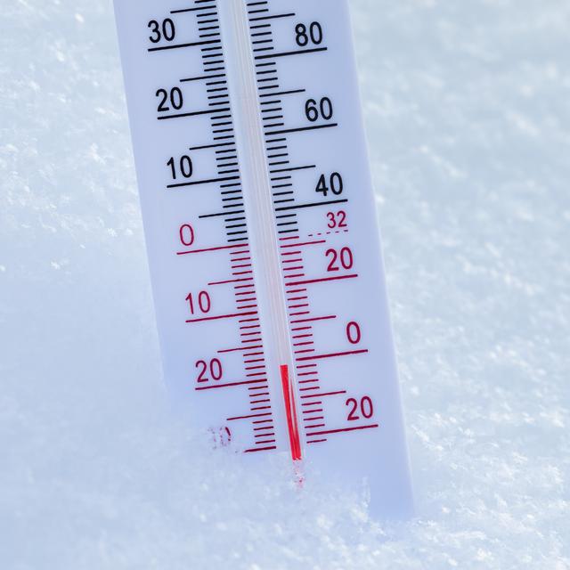 White outdoor thermometer standing in fresh snow with the red column showing a temperature well below freezing