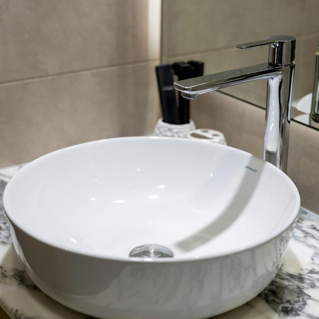 White round vessel sink with a tall chrome faucet on a marble vanity