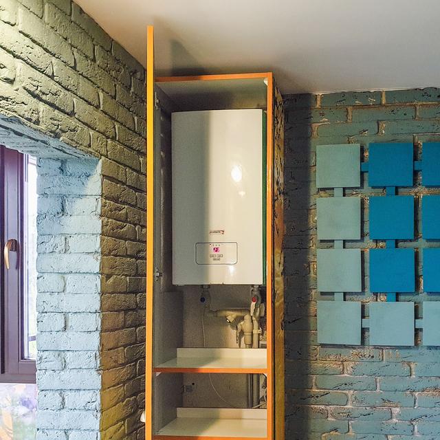 Compact wall-mounted water heater installed in a cabinet niche with water and gas connections below