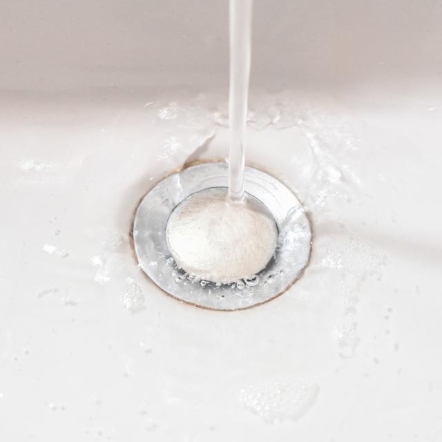 Stream of water running from a faucet into a white sink drain