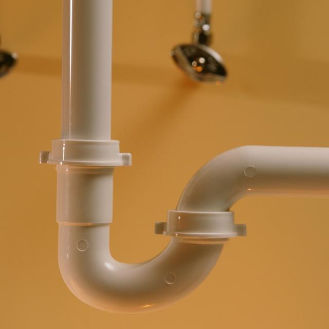 White PVC P-trap under a sink against a tan wall